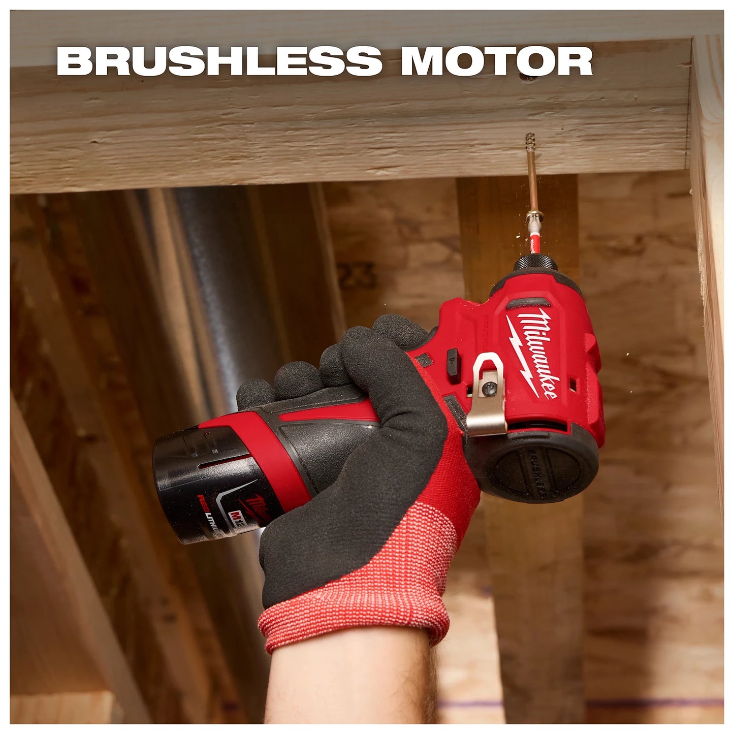 A gloved hand holds a Milwaukee brushless motor drill, screwing a fastener into a wooden beam within a construction area.
