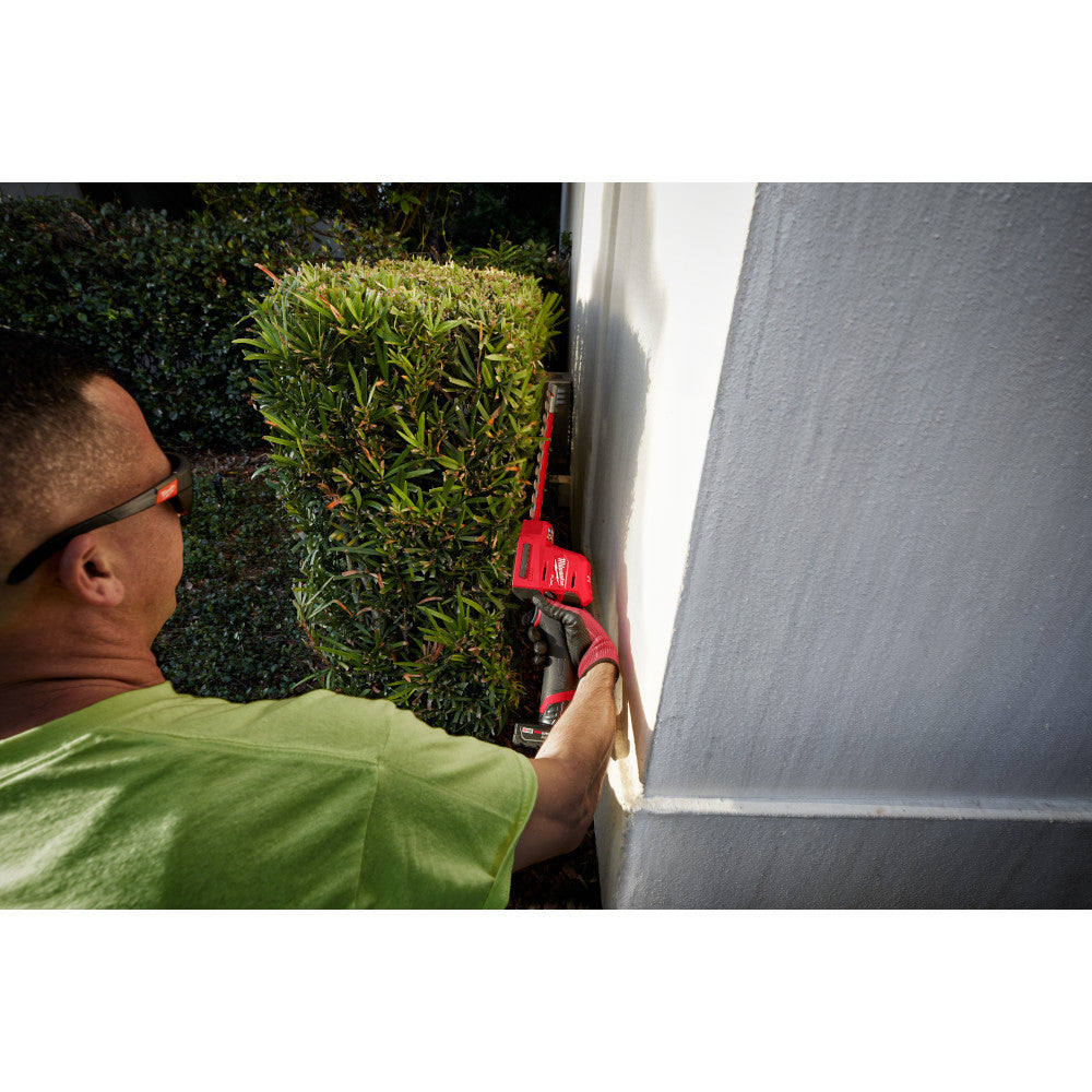 Milwaukee 2533-20 12V FUEL 8in Hedge Trimmer (Tool Only) showing in use cutting hedges directly next to a wall (Battery Sold Separately)