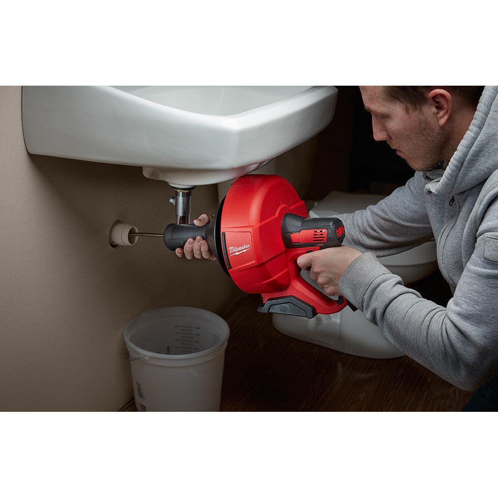 Milwaukee 2571-21 M12 Cordless Auger Drain Snake with 5/16 inch Cable Kit showing in use clearing drain under a sink