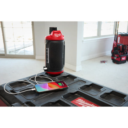 Milwaukee 2955-20 12V Bluetooth Jobsite Speaker with PACKOUT Compatibility (Tool Only) showing in use mounted to a packout box  while charging a phone