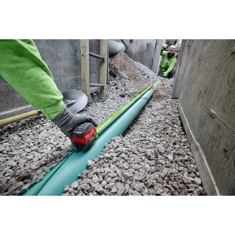 Milwaukee 48-22-1425 25ft Stud Tape Measure showing in use measuring a pipe partial buried in gravel