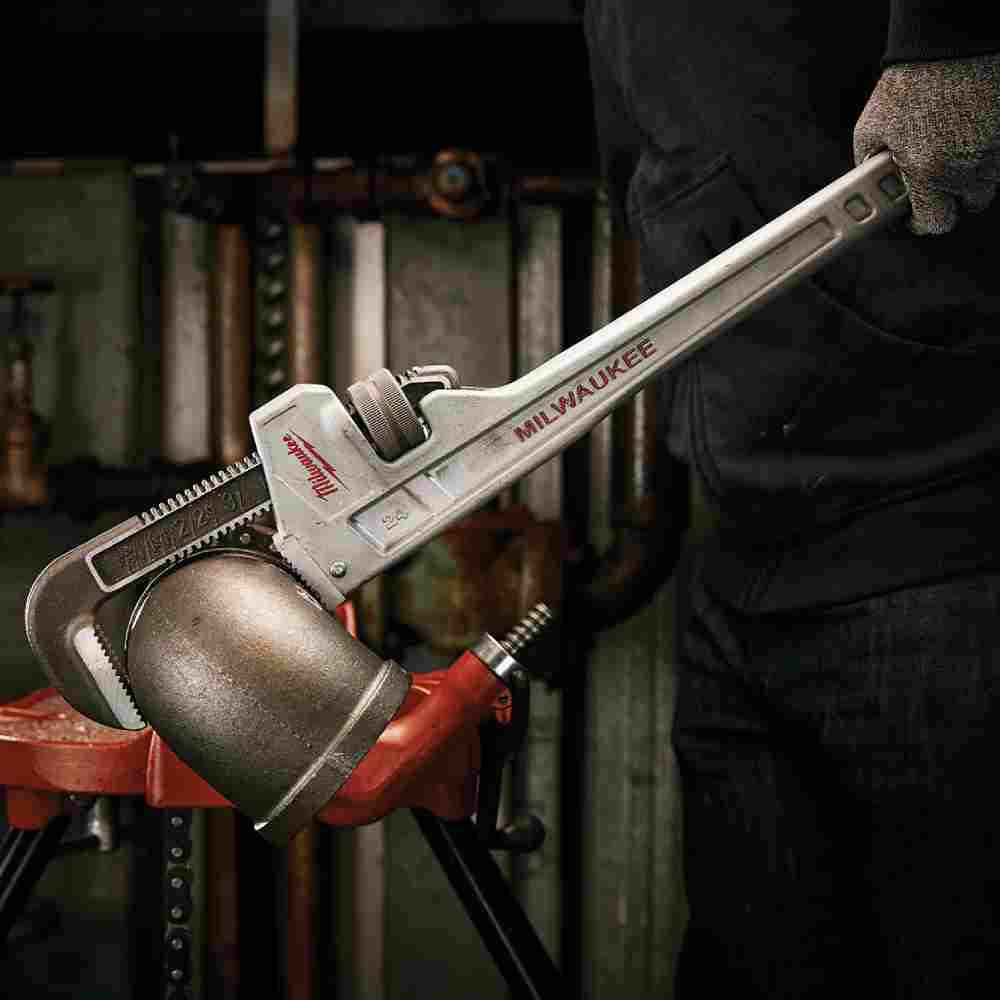 Milwaukee 48-22-7224 24 inch Aluminum Pipe Wrench showing wrench in use tightening an elbow on a length of pipe while strapped to a work bench