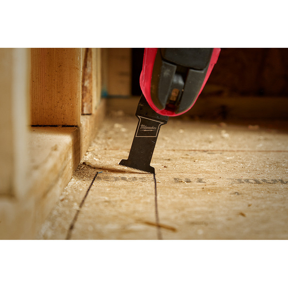 Milwaukee 49-25-1101 OPEN-LOK 1-3/8 inch Universal Fit High Carbon Steel Wood Cutting Multi-Tool Oscillating Blade showing in use cutting hole in wooden sub-floor