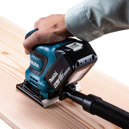 Makita DBO480ZX1 18V LXT Cordless 1/4 Sheet Finishing Sander (Tool Only) showing in use sanding a wood plank with vacuum hose attached (Vacuum sold separately)