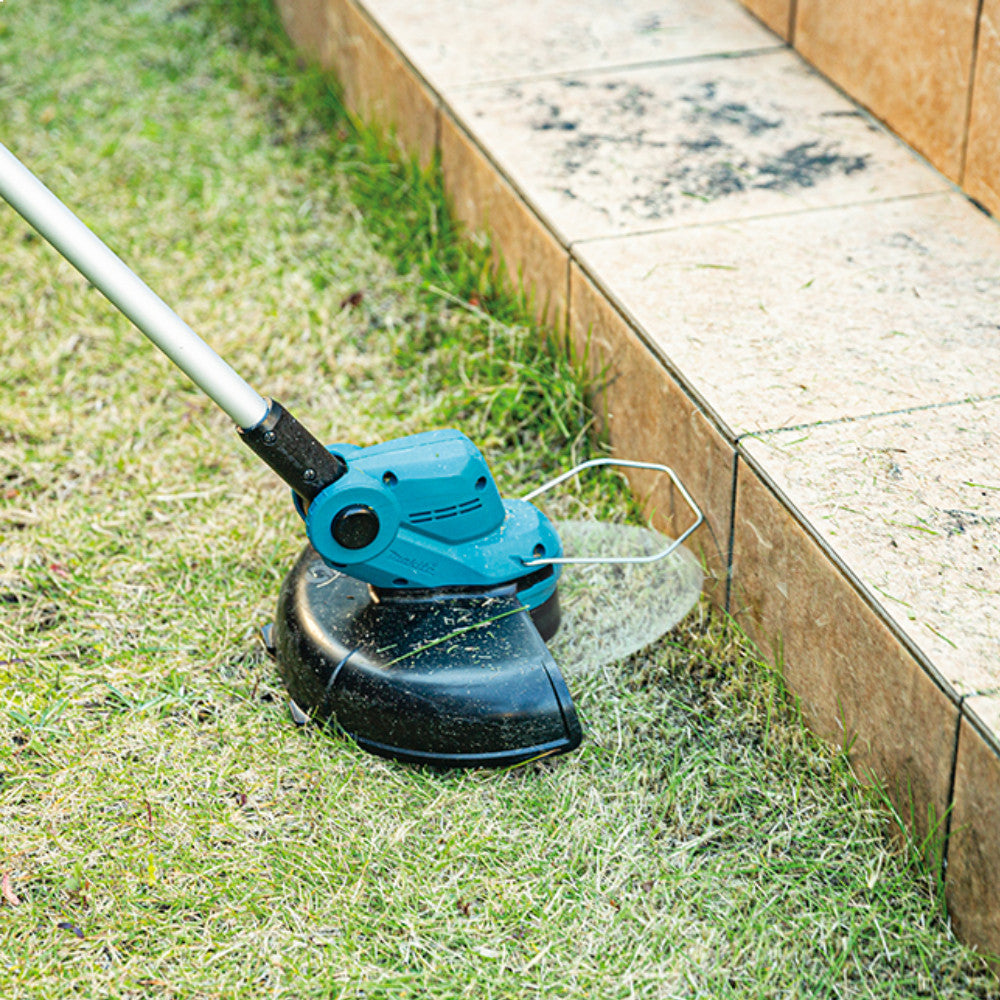 Makita DUR193Z 18V LXT Cordless 10-1/4 inch Line Trimmer (Tool Only) showing in use cutting grass allow wooden boarder