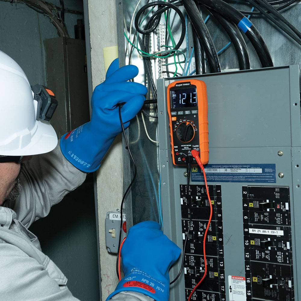 Klein Tools MM720 1000V TRMS Auto-Ranging Digital Multimeter showing in use testing voltage with clamp while being mounted to a electrical panel