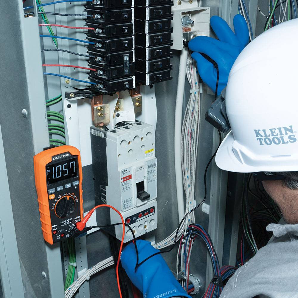 Klein Tools MM720 1000V TRMS Auto-Ranging Digital Multimeter showing in use testing voltage with clamp while being mounted to a electrical panel