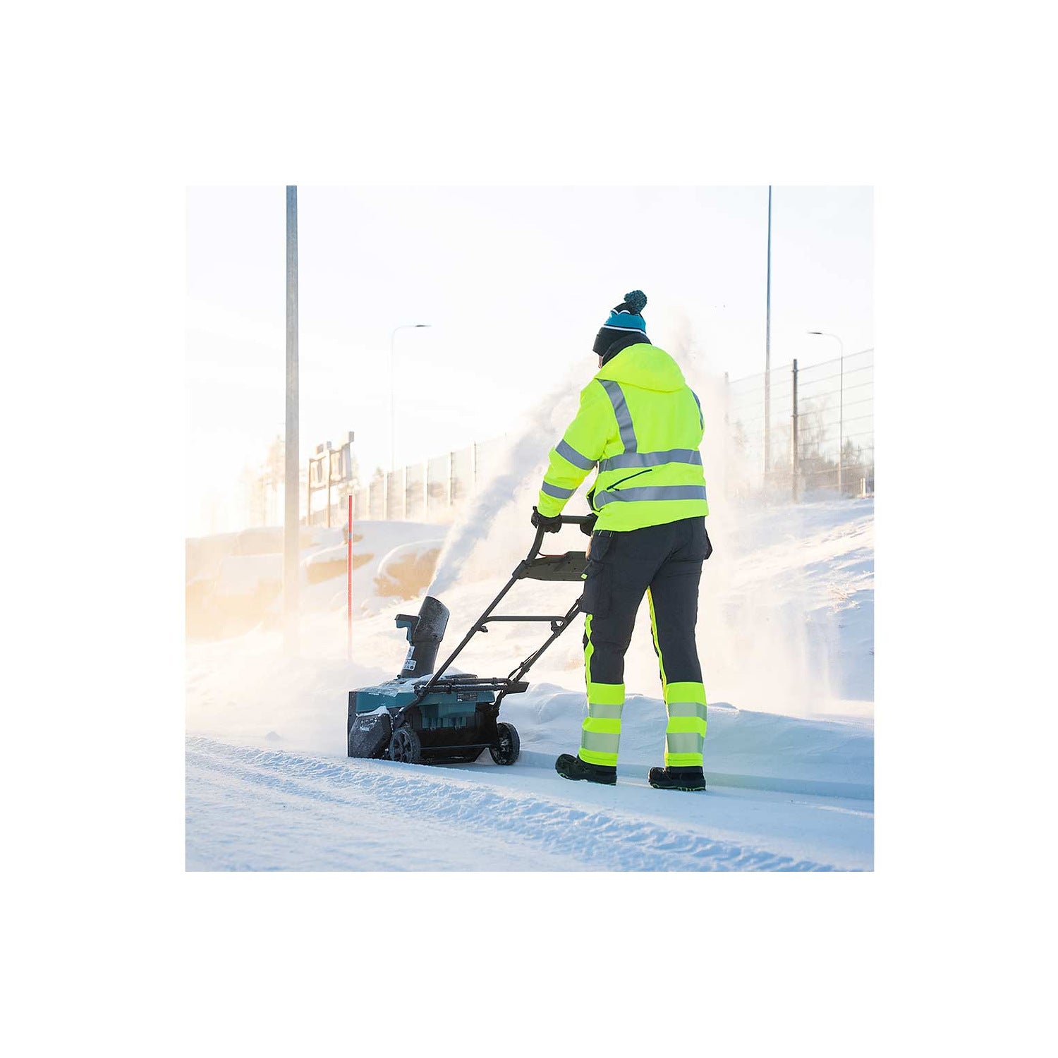 Makita SN001G snow blower clearing a snowy roadway from the rear