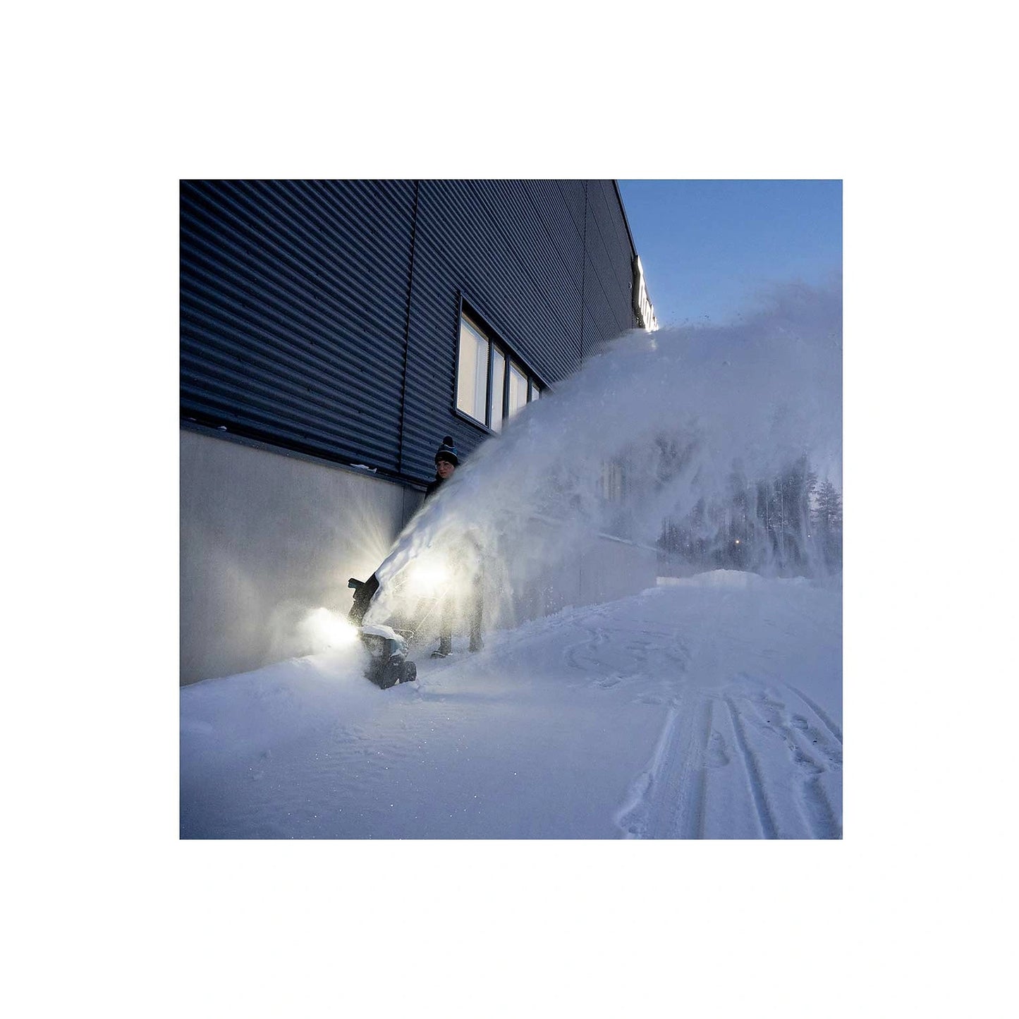 Makita SN001G snow blower throwing deep snow near a building