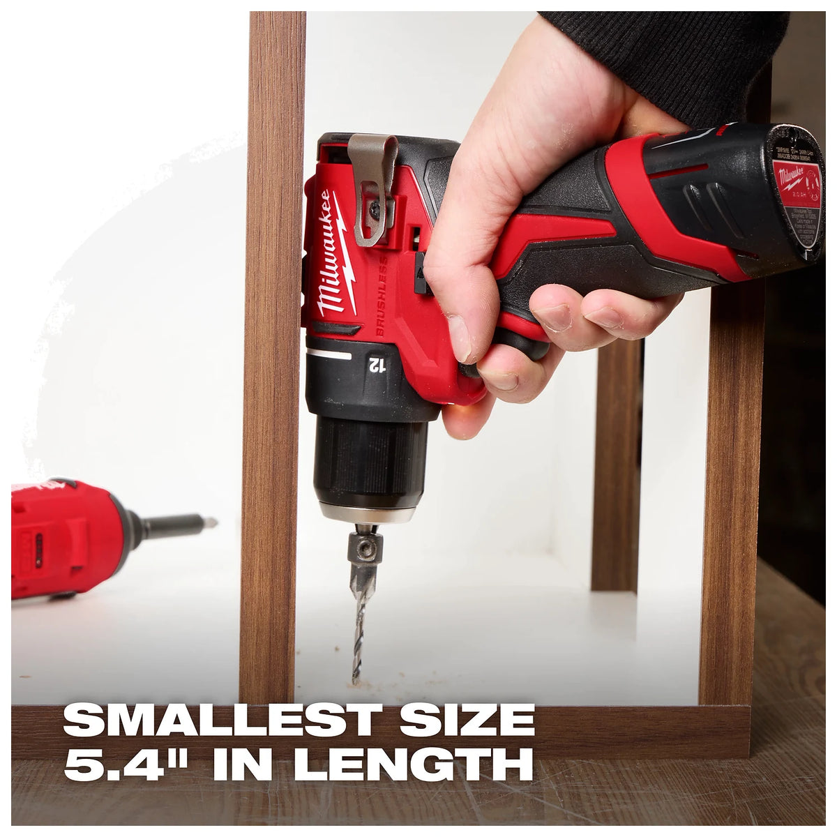 A hand grips a red and black Milwaukee cordless drill with a drill bit attached. "Smallest size 5.4" in length" is written at the bottom. Another red drill lies in the background.