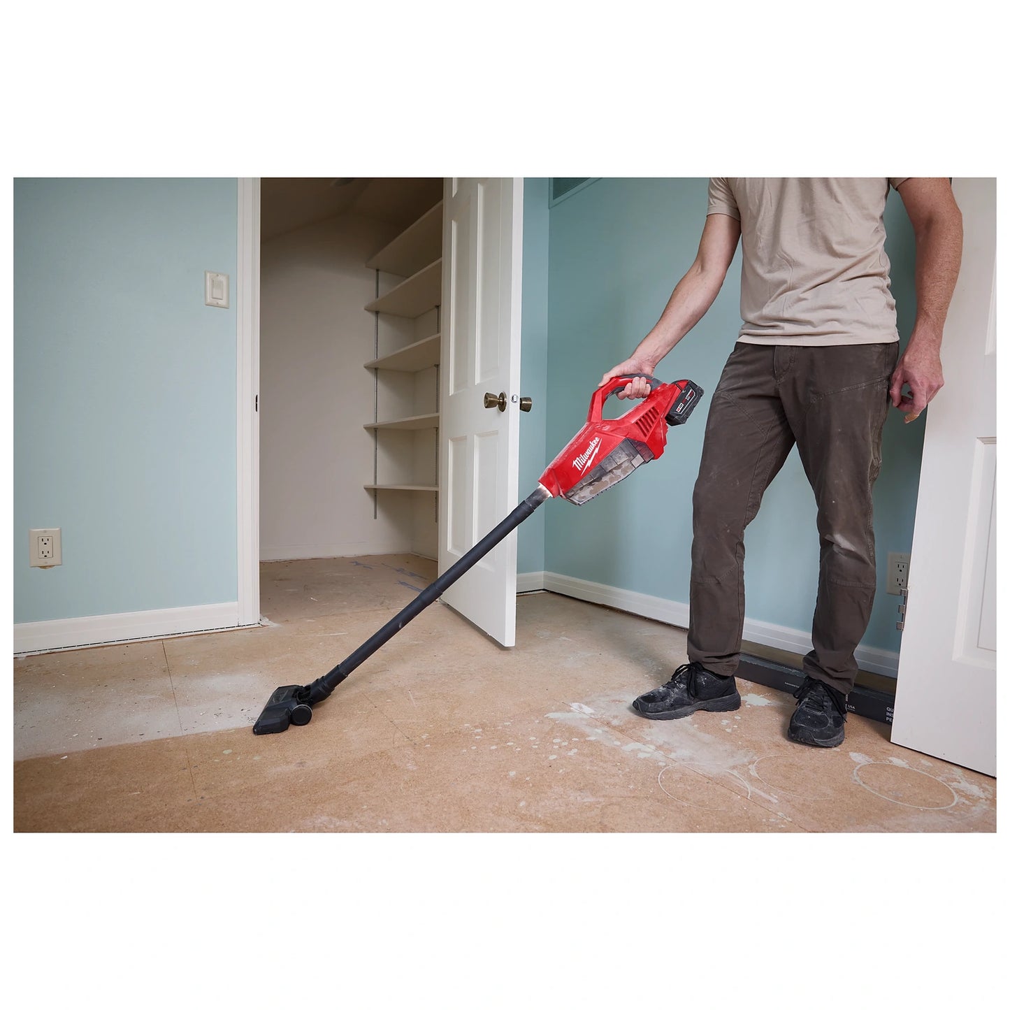 A person vacuums a dusty floor using an M18 Brushless Handheld Vacuum in a partially renovated room.