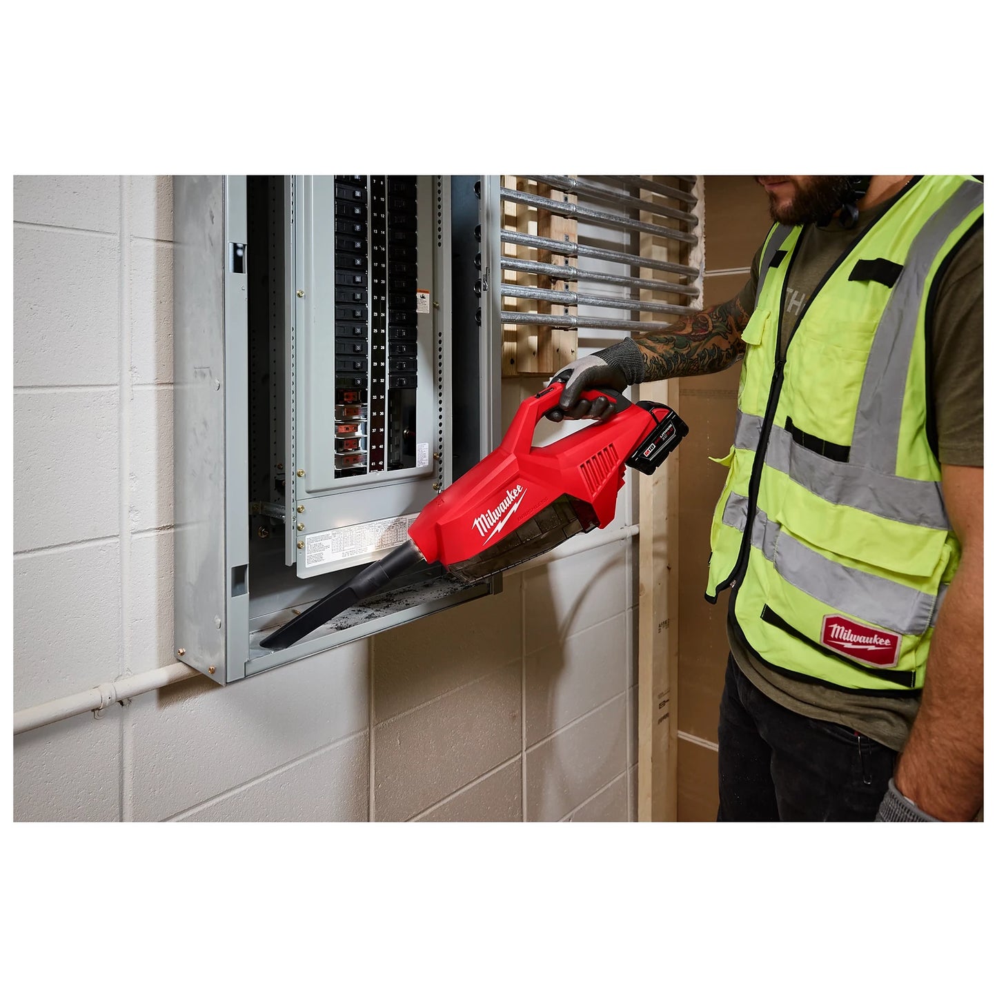 A worker uses the red M18 Brushless Handheld Vacuum to clean dust from an electrical panel. The vacuum is battery-operated and branded with the Milwaukee logo.