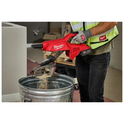 A person is emptying dust from the M18 Brushless Handheld Vacuum into a metal trash can.