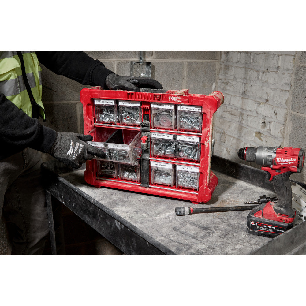 Person organizing tools in a red Milwaukee tool chest with a drill on a concrete floor.