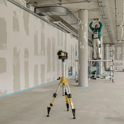Construction site with a laser level on a tripod and a worker on a ladder.